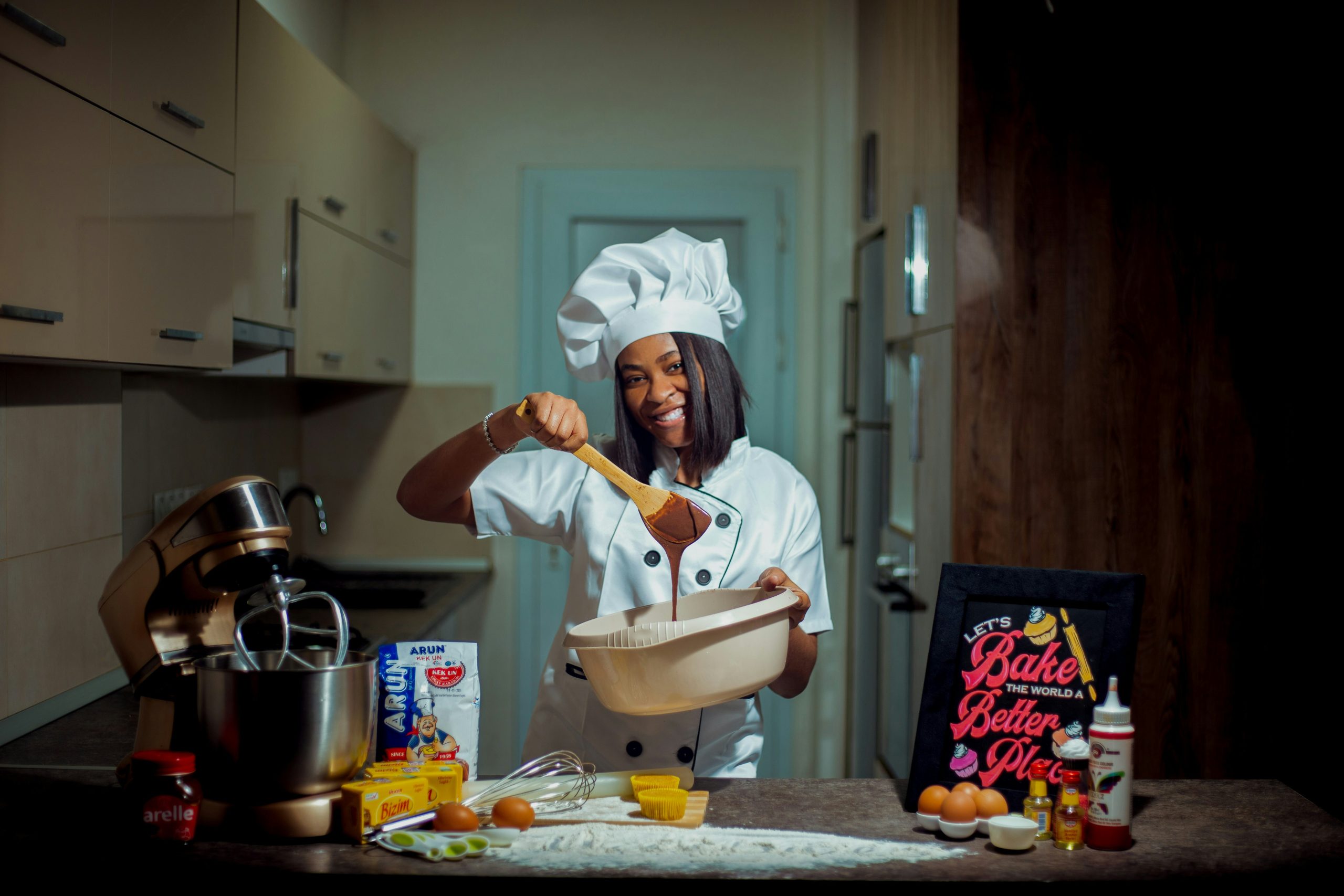 chef showing her skills at mixing batter in a kitchen iwth a stand mixer smiling. Photo by <a href="https://unsplash.com/@official_umoh?utm_content=creditCopyText&utm_medium=referral&utm_source=unsplash">Emediong Umoh</a> on <a href="https://unsplash.com/photos/a-woman-in-a-chefs-hat-holding-a-wooden-spoon-fY9ZV9-475o?utm_content=creditCopyText&utm_medium=referral&utm_source=unsplash">Unsplash</a><br />
      